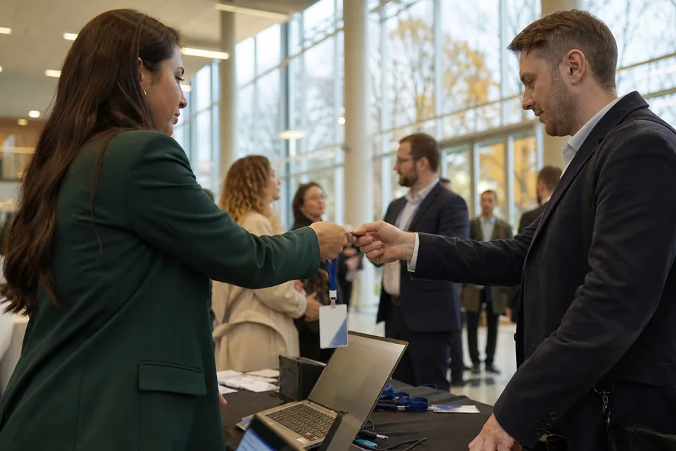Hostessa w zielonym żakiecie wydaje identyfikator gościowi przy stanowisku rejestracji w holu centrum konferencyjnego